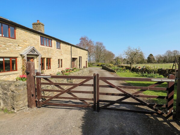 A stone building with a gated entrance, a stone wall, and a pathway leading to a green field.