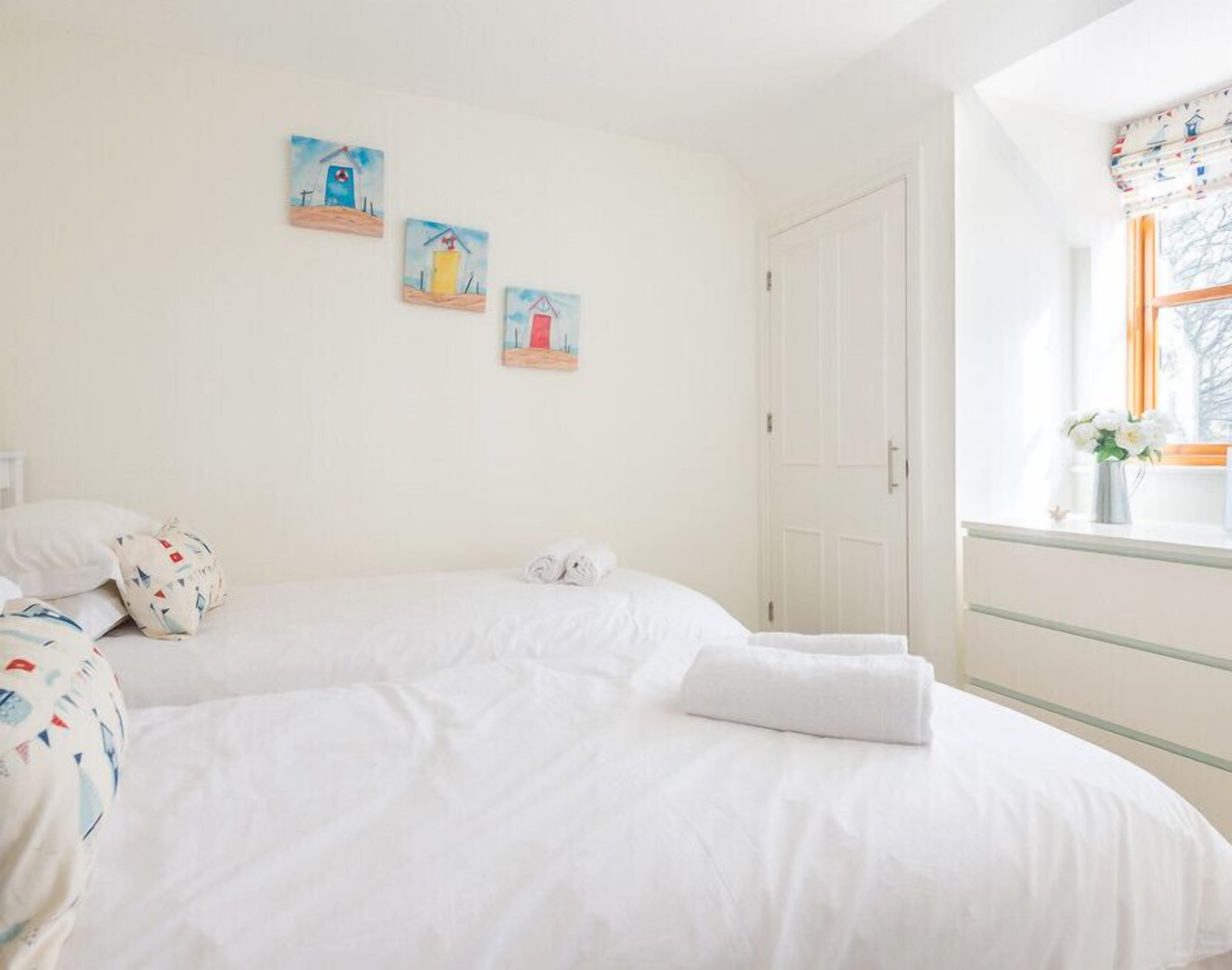 Une chambre avec deux lits, une fenêtre avec des rideaux et trois tableaux accrochés au mur.