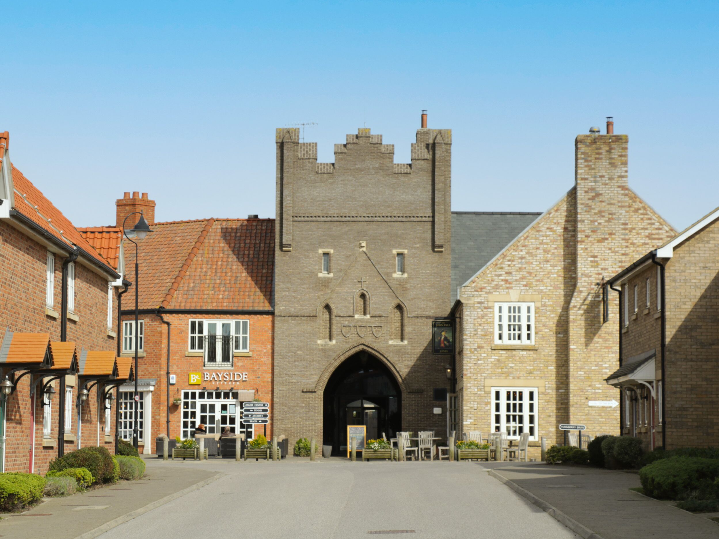 A historic building with a central tower, a sign for Bayside Kitchen, and a paved courtyard with benches.