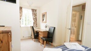 Une chambre à coucher comprenant un lit, un bureau, deux chaises, un radiateur, une fenêtre avec des rideaux et une porte.