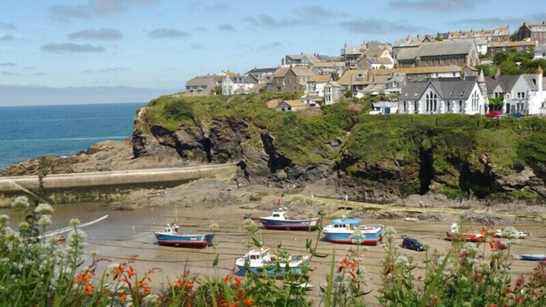 Un pueblo costero con barcos en la orilla, casas en un acantilado y una vista despejada del mar.