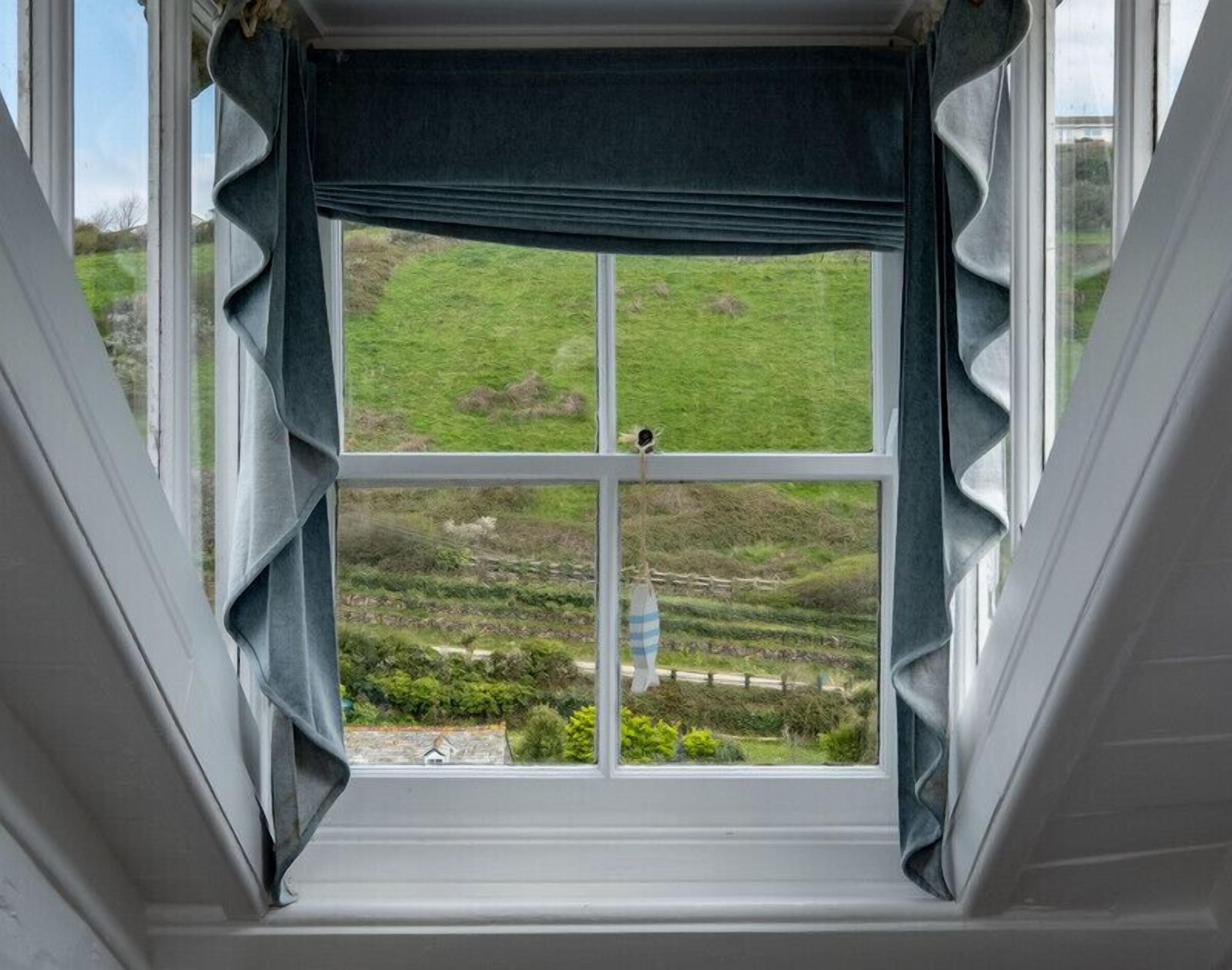 Una ventana con vistas a un paisaje verde, que incluye campos y una cerca.
