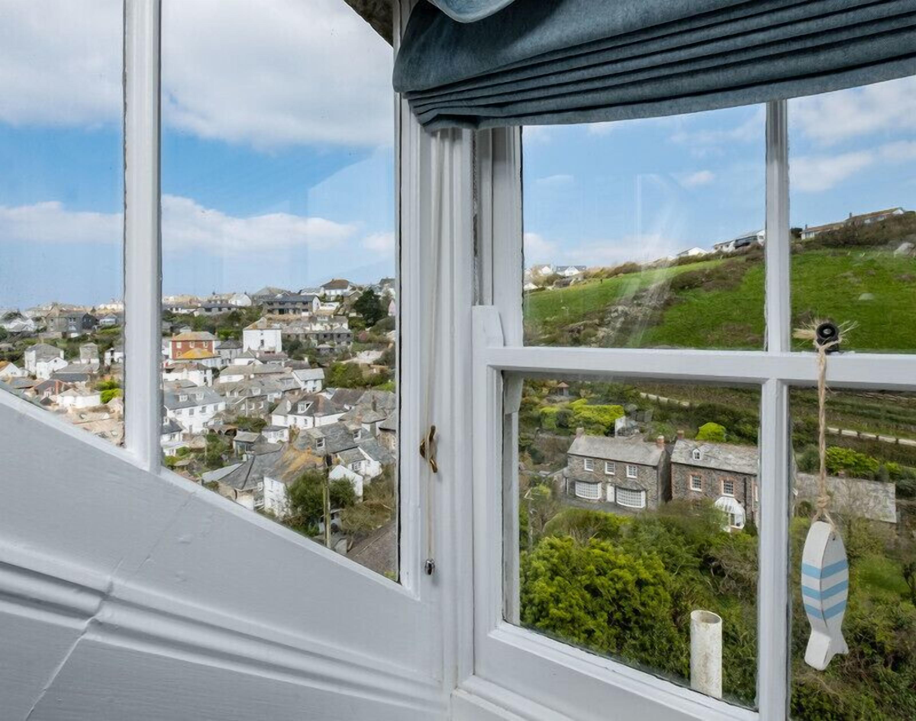 A view from a window overlooking a coastal town with houses and greenery.