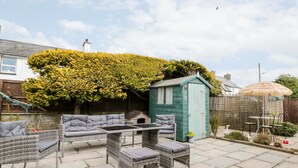 Une terrasse avec des meubles en osier, un petit abri de jardin et un arbre aux feuilles jaunes.