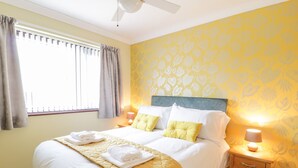 Un lit bien fait, recouvert d’une couette jaune, avec deux oreillers et des serviettes pliées, le tout posé sur un tapis beige.