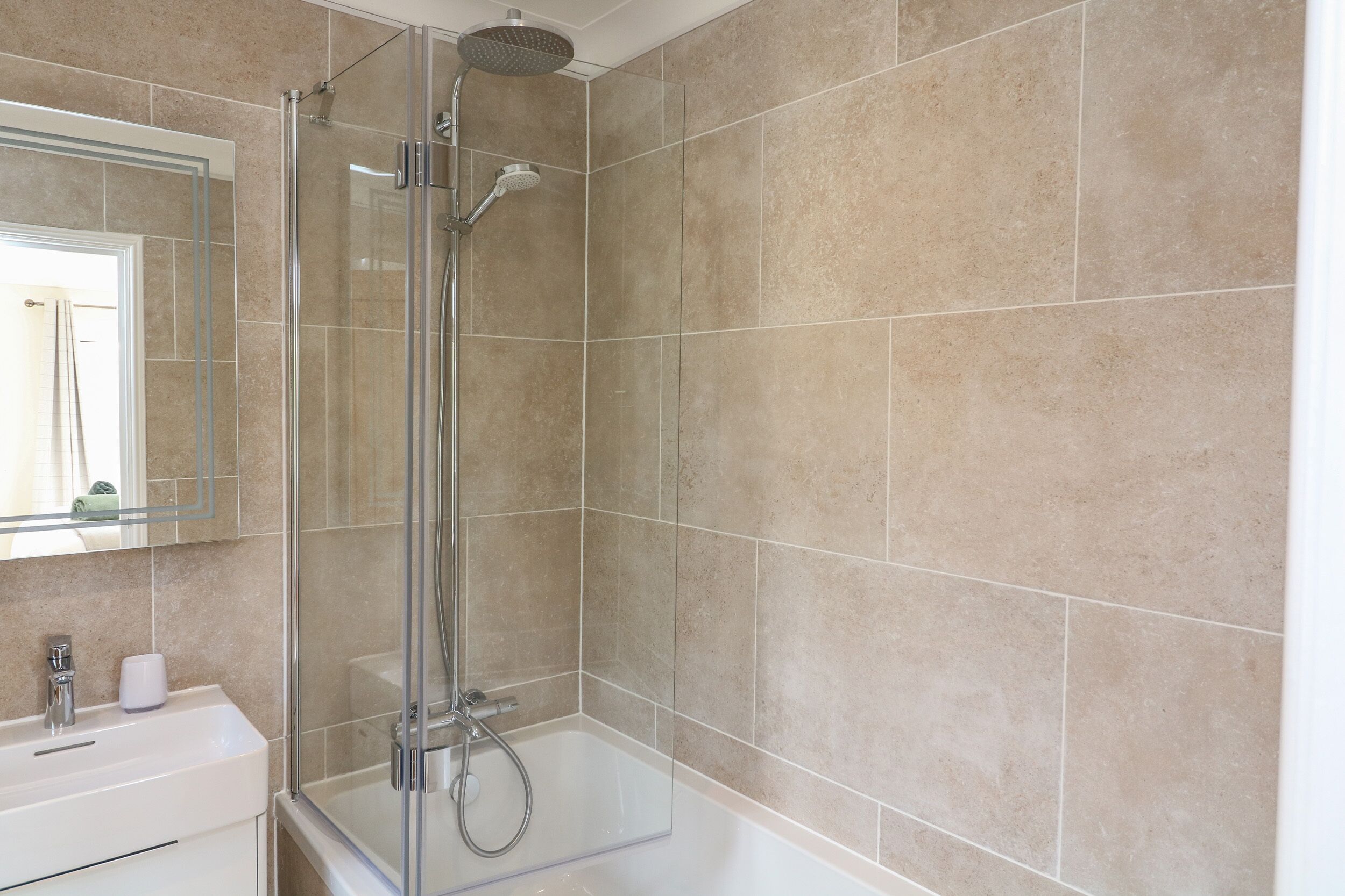 A modern bathroom with a glass-enclosed shower, a white sink, and beige tiles.