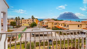 A coastal residential area with buildings, a balcony, and a mountain in the background. - Il Vecchio Faro A42 150m From The Beach (Loiri Porto San Paolo)