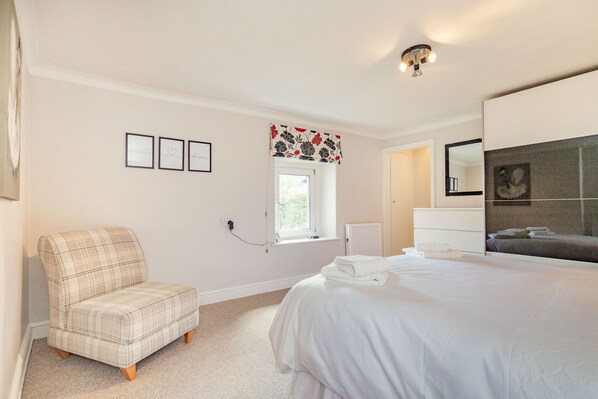 A bedroom with a bed, a chair, a window, and a mirror.