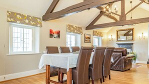 A dining area with a table set for six, wooden beams on the ceiling, and a fireplace with a mirror above it. - Dales Croft Apartment (Buxton)