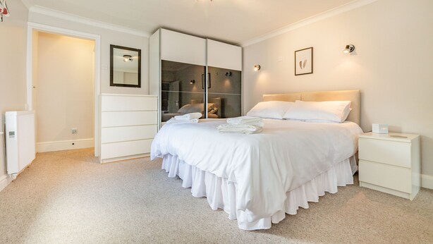 A bedroom with a large bed, a wardrobe, a bedside table, and a mirror on the wall. - Dales Croft Apartment (Buxton)
