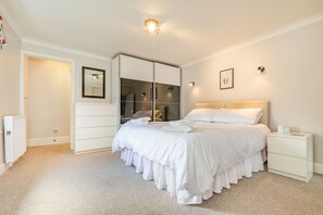 A bedroom with a large bed, a wardrobe, a bedside table, and a mirror on the wall.