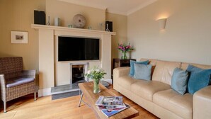 A living room with a fireplace, a sofa, a coffee table, and a television. - Worthy House (Wadebridge)