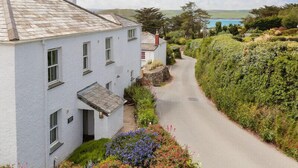 A white building with a sloped roof, a narrow road leading to it, and lush greenery on the right. - Worthy House (Wadebridge)