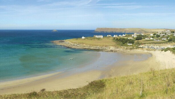 A coastal landscape with a sandy beach, a small island, and a cluster of white buildings. - Worthy House (Wadebridge)
