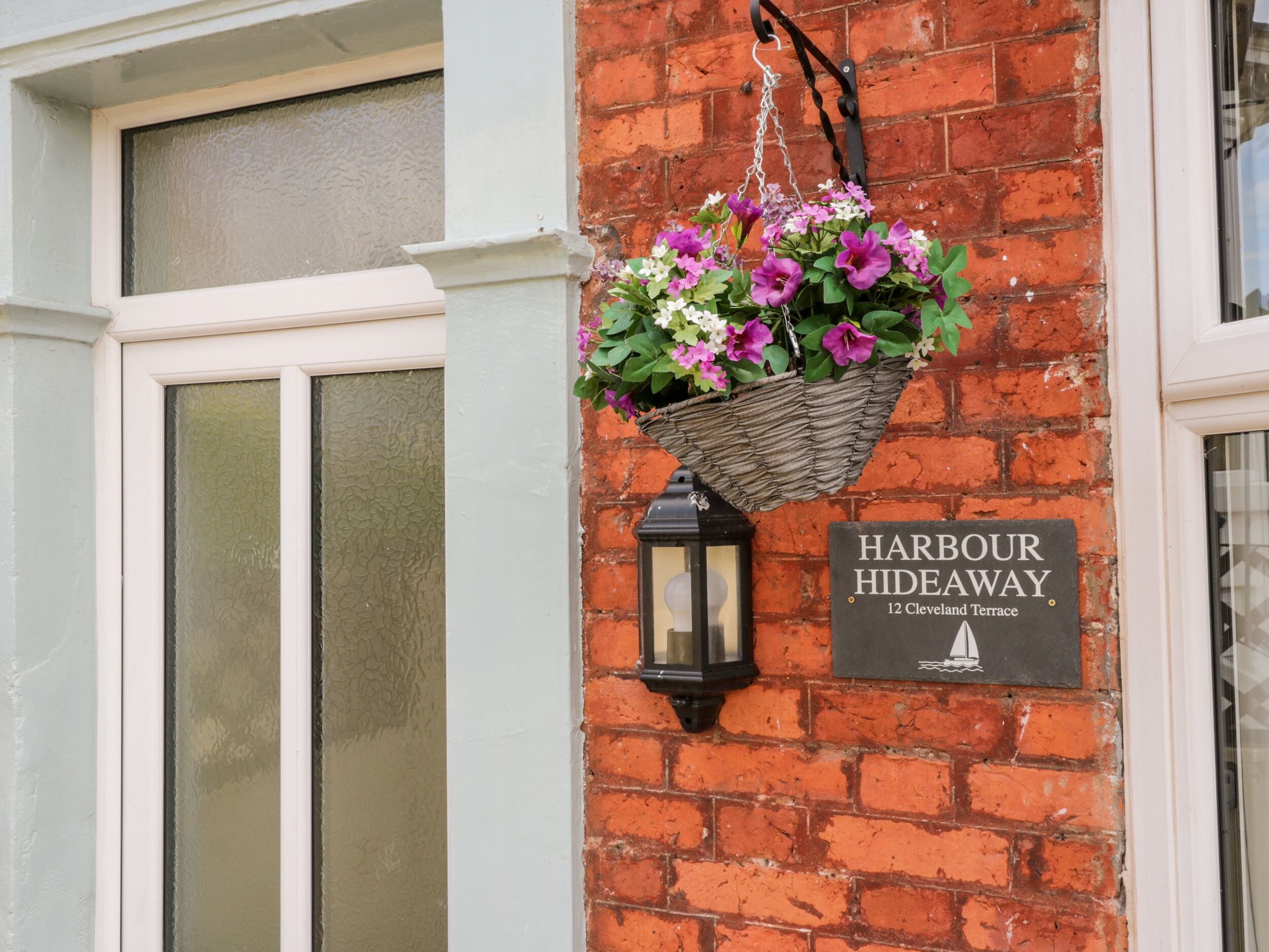 A brick wall with a hanging flower basket and a sign reading "Harbour Hideaway 12 Cleveland Terrace".