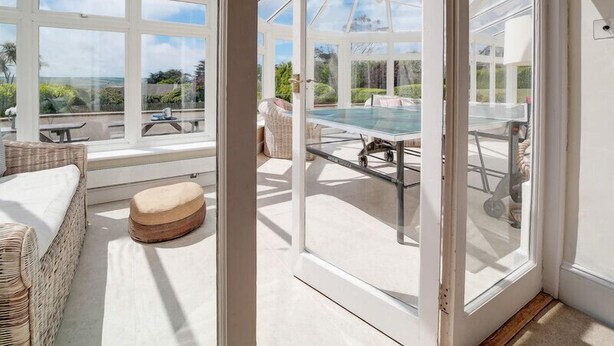 A conservatory with a glass table and chairs, a cushioned bench, and a view of the outdoors. - The Haven (Wadebridge)