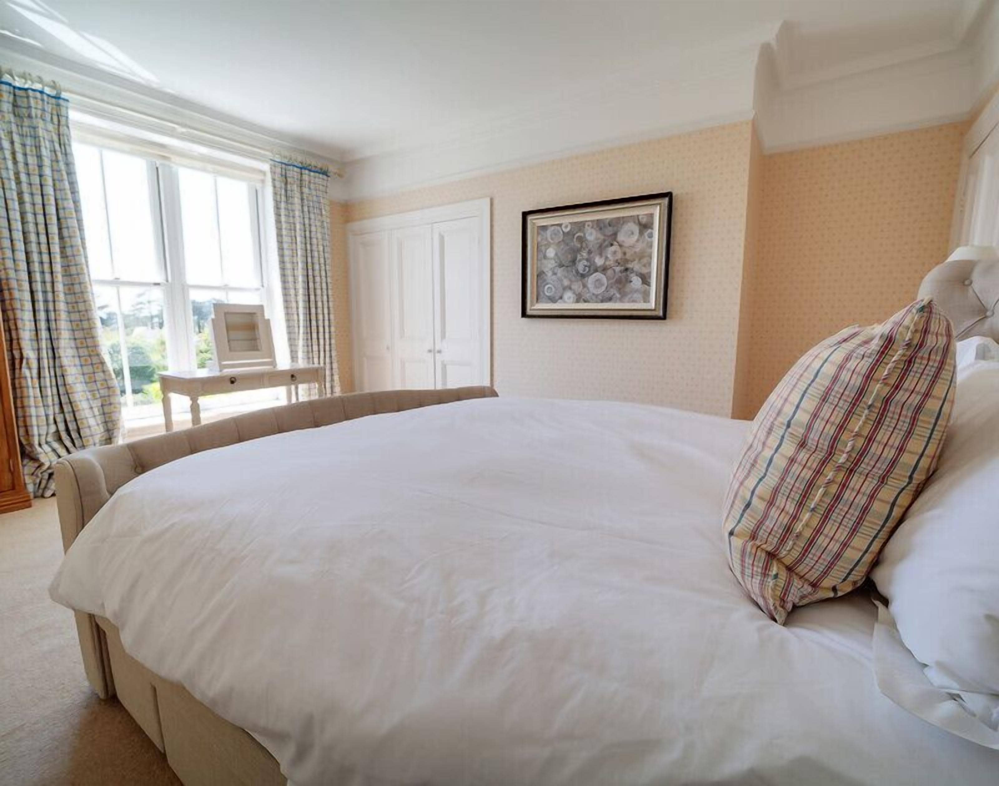 A large bed with white linens, a plaid pillow, and a framed picture on the wall.