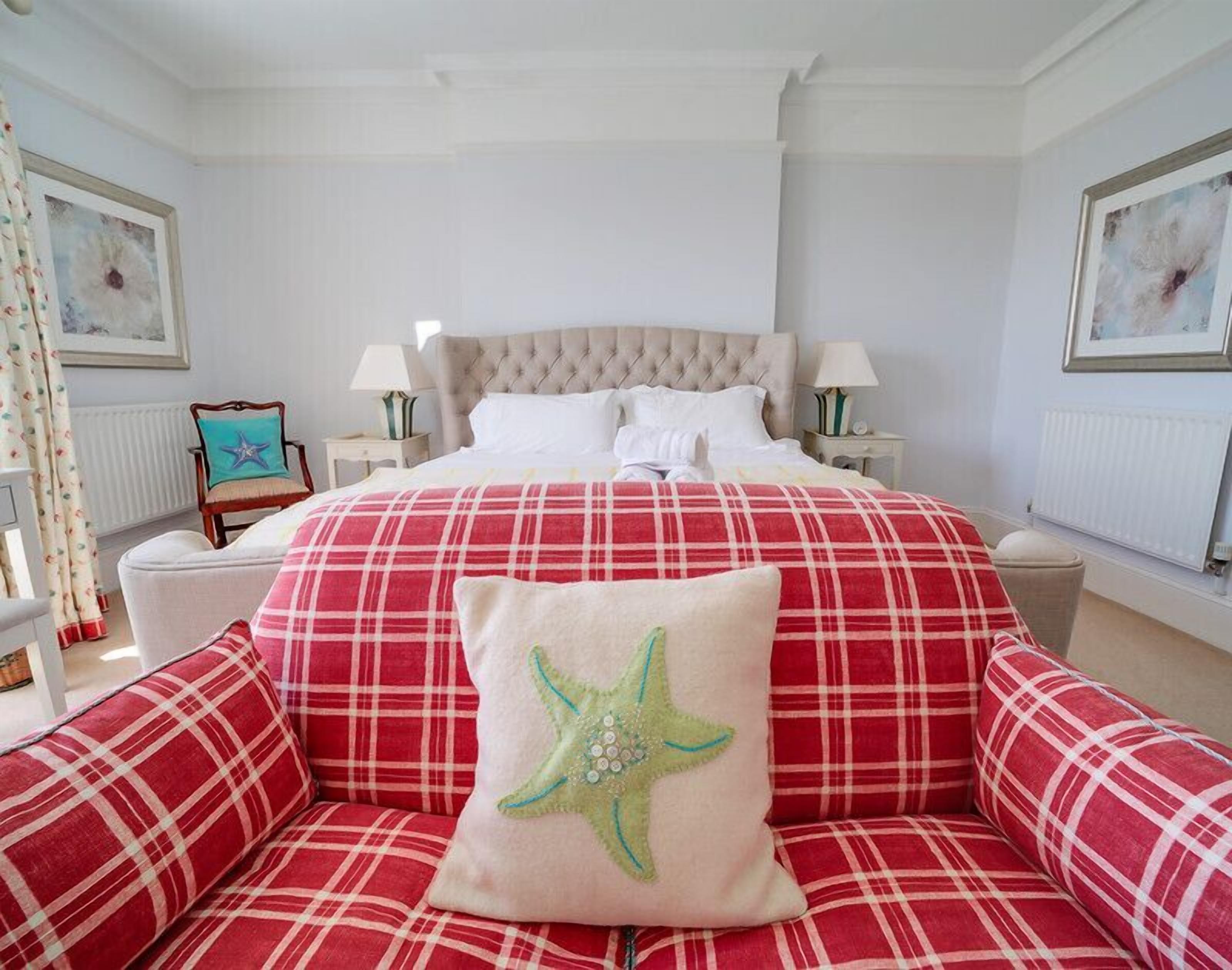 Une chambre avec un grand lit, deux tables de chevet, une chaise et un coussin en forme d’étoile de mer.