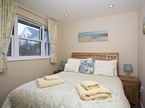 Quarto com cama, duas mesas de cabeceira, janela com cortinas e um quadro na parede.