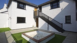 A two-story house with a white exterior, a black staircase, and a rectangular garden area with white pebbles and green grass. - Crowthers (Dartmouth)