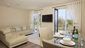 A modern living room with a sofa, a glass dining table set for two, and a TV mounted on the wall. - Crowthers (Dartmouth)