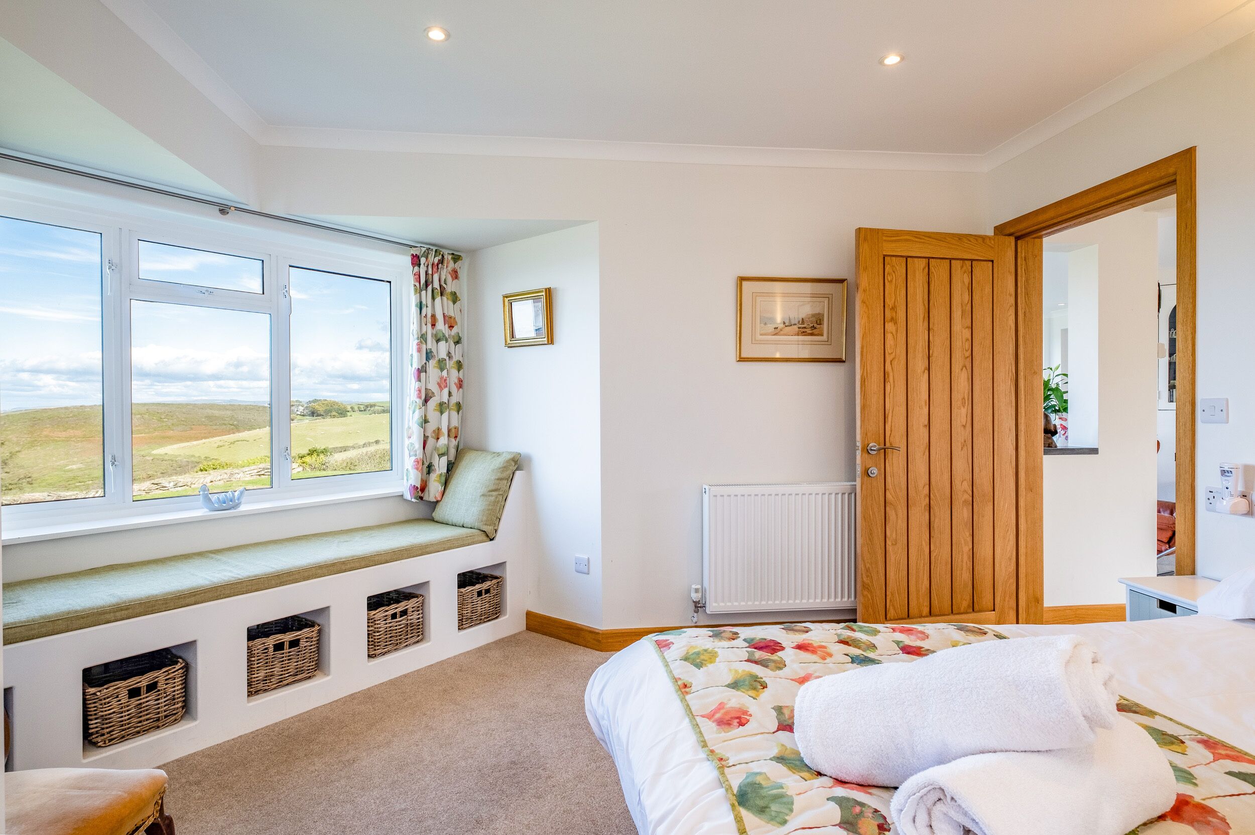 A bedroom with a large window, a wooden door, and a bed with a floral bedspread.
