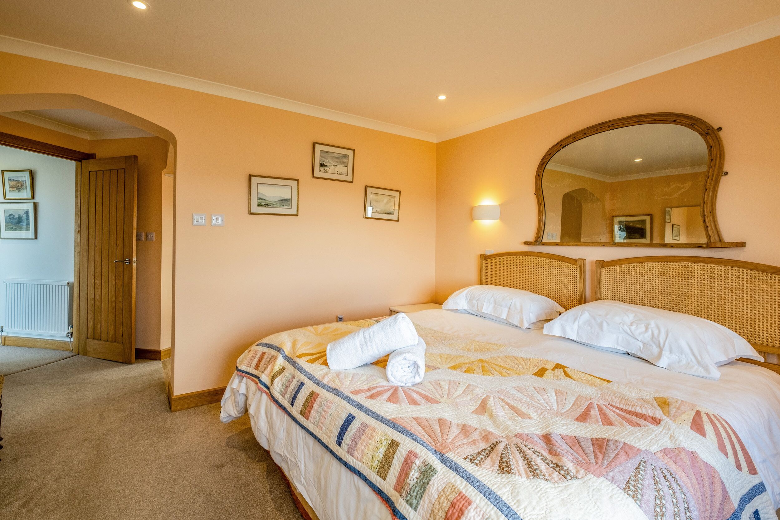A hotel room with a large bed, a wooden headboard, a wall-mounted mirror, and a door leading to another room.