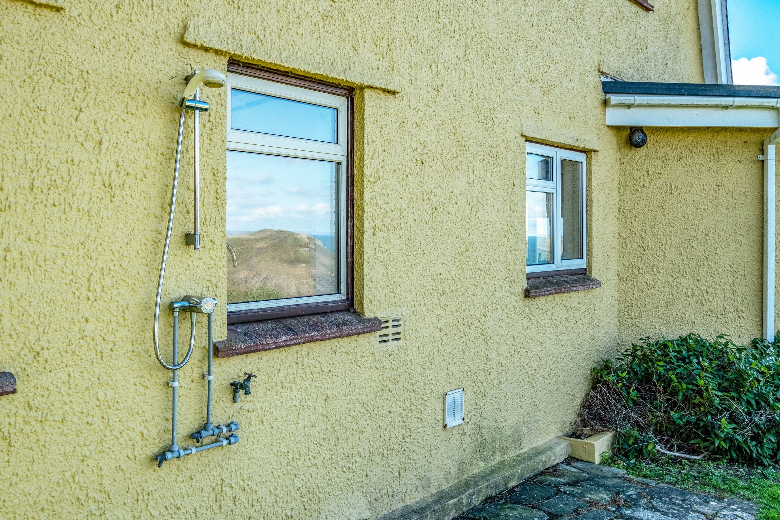 A building with a window, a showerhead, and a small window above the showerhead.
