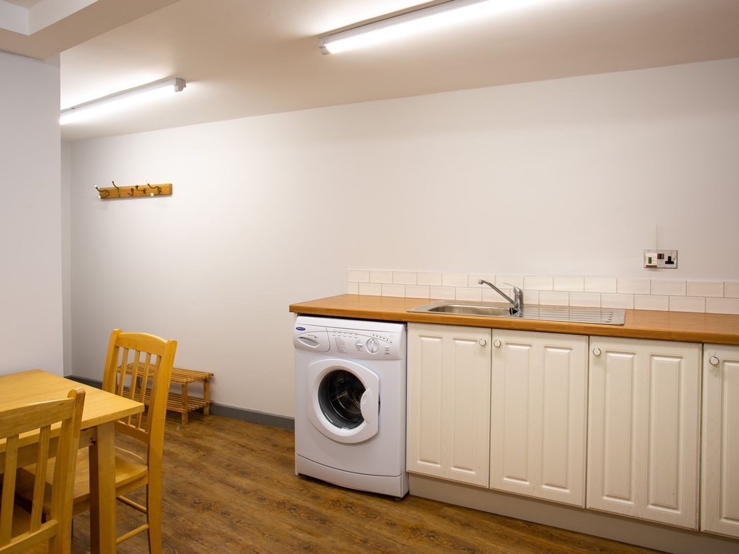 A compact kitchen with a built-in washer, a wooden dining table, and white cabinets.