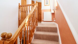 Un escalier avec des balustrades en bois et des marches recouvertes de moquette, menant à un palier où se trouvent un radiateur et un tableau encadré accroché au mur.