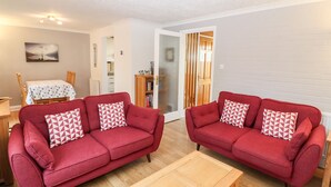 Un salon avec deux canapés rouges, une table basse en bois et un coin repas comprenant une table et des chaises.