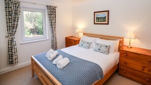 Une chambre à coucher avec un lit en bois, deux tables de chevet avec des lampes, une fenêtre avec des rideaux et un tableau encadré au mur.