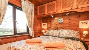 A wooden cabin bedroom with a bed, curtains, and a window. - Holly Lodge (Saltburn-by-the-Sea)