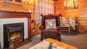 A cozy room with a fireplace, a plaid armchair, a dining table with chairs, and a painting on the wall. - Holly Lodge (Saltburn-by-the-Sea)