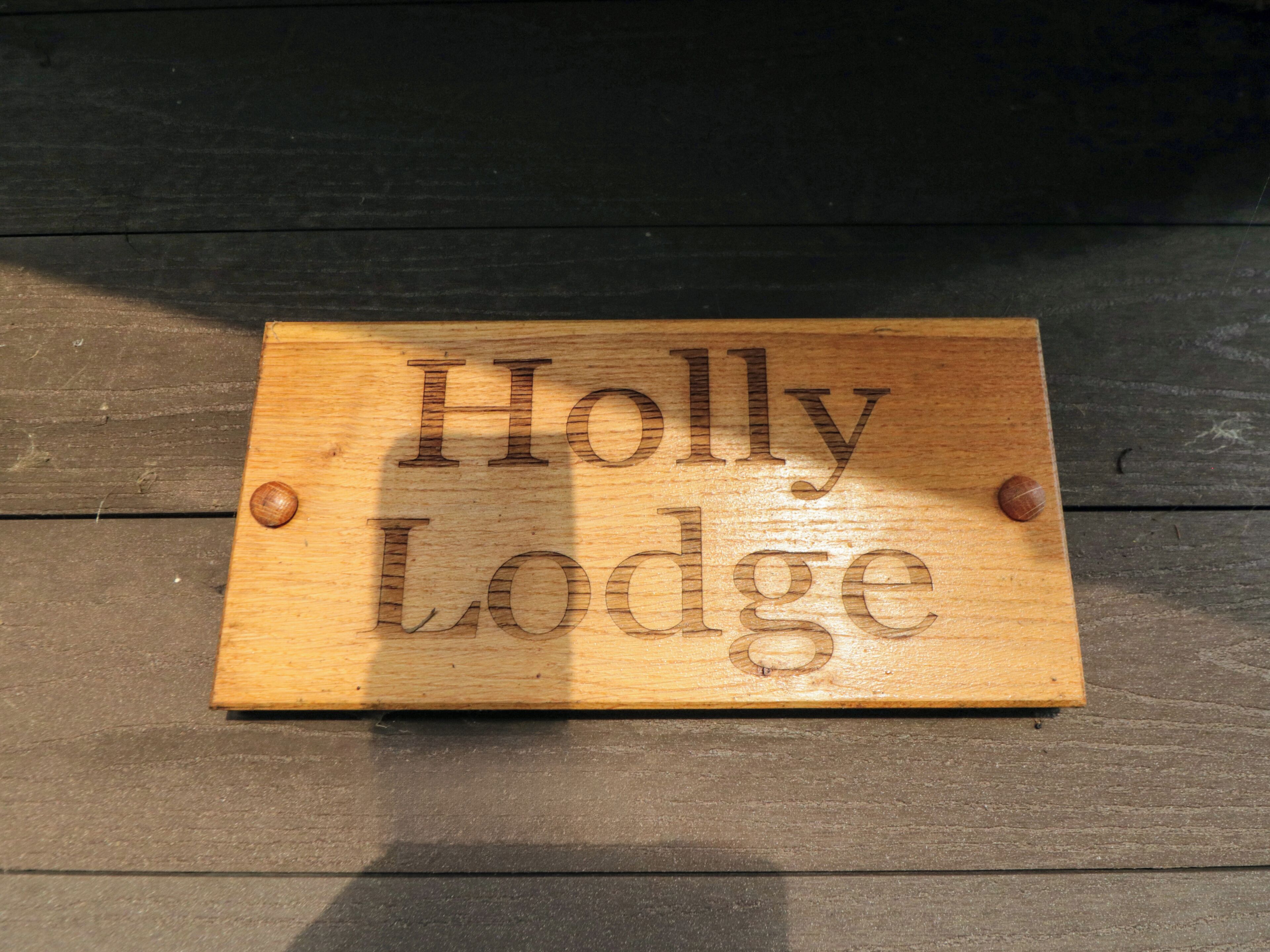 A wooden sign with the text "Holly Lodge" mounted on a wooden surface.