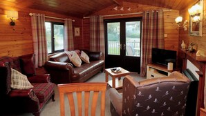 A cozy cabin interior with a leather sofa, a wooden chair, a television, and a fireplace. - Holly Lodge (Saltburn-by-the-Sea)