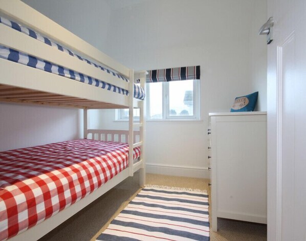 A bunk bed room with a checkered red and white bedspread, a striped rug, and a white cabinet.