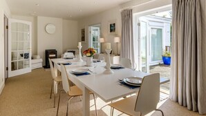 A dining room with a white table set for four, a fireplace, and a view of the garden through the glass door. - The Moorings (Wadebridge)