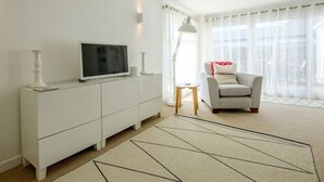 A modern living room with a white TV on a cabinet, a grey sofa, and a patterned rug. - The Moorings (Wadebridge)
