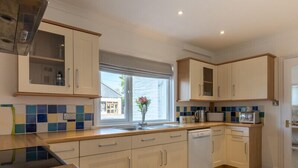 A modern kitchen with white cabinets, a dishwasher, and a window with a view of the outside. - The Moorings (Wadebridge)