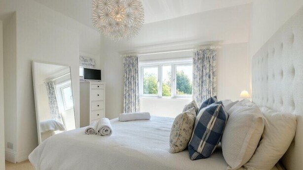 A bedroom with a large bed, a dresser, a television, and a window with curtains. - The Moorings (Wadebridge)
