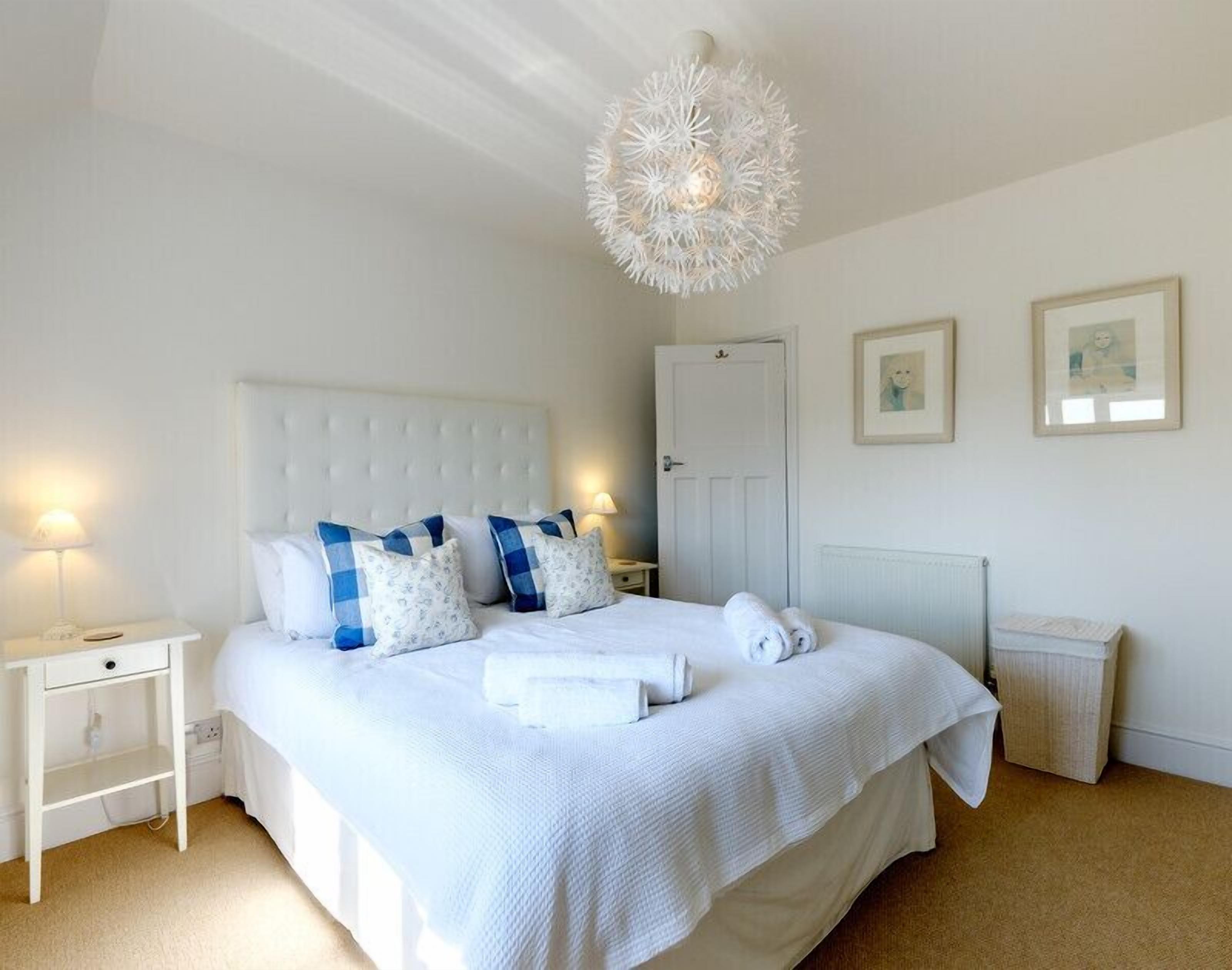 Une chambre à coucher bien aménagée, avec un grand lit, du linge de lit blanc, une table de chevet avec une lampe et un luminaire au plafond original.