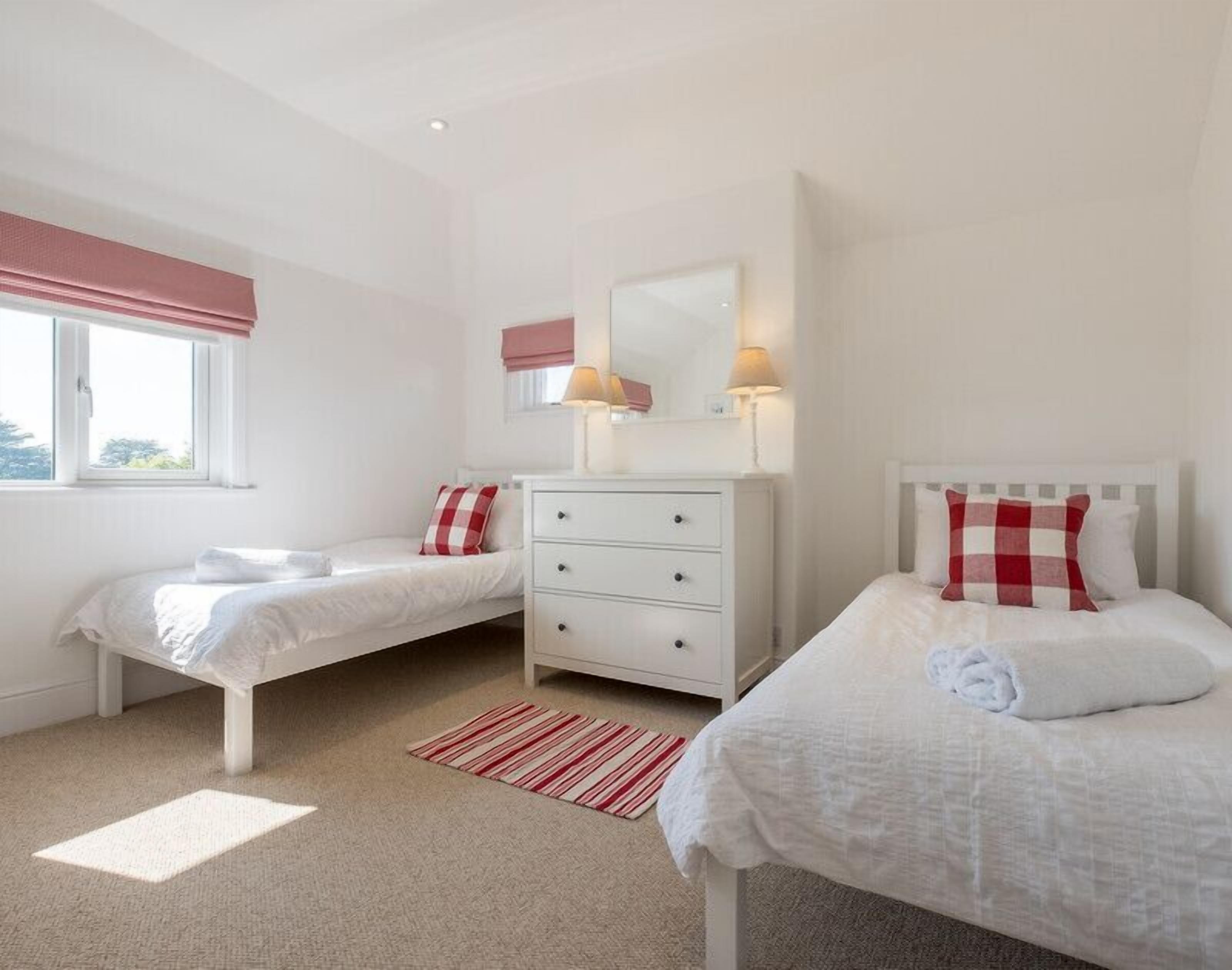 A bedroom with two single beds, a white dresser, a mirror, and a window with curtains.