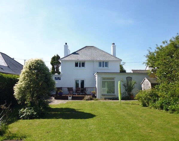 A two-story house with a front porch, a small garden, and a garage. - The Moorings (Wadebridge)