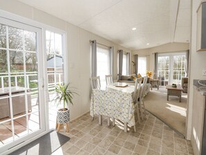 A spacious dining area with a large table and chairs, a potted plant, and a view through glass doors to an outdoor patio. - Lakeside View (King's Lynn)