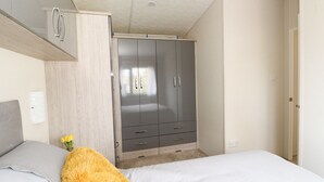 Quarto com cama, guarda-roupa e uma pequena mesa com um vaso de flores.