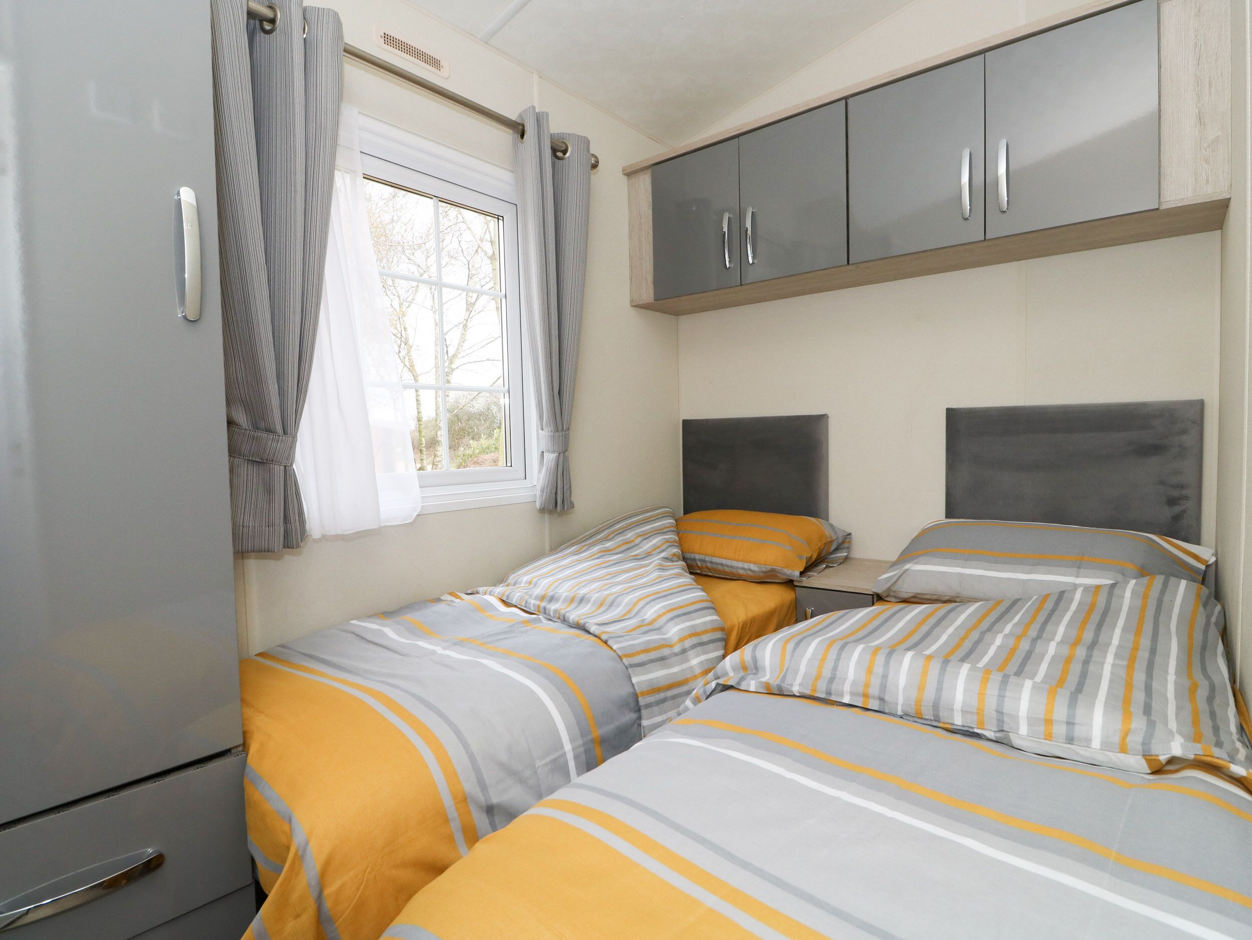 Een knus slaapkamer met twee bedden, grijze kasten, een raam met gordijnen en een kleine garderobe.