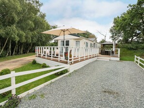 A white wooden cabin with a deck and a covered outdoor seating area. - Lakeside View (King's Lynn)