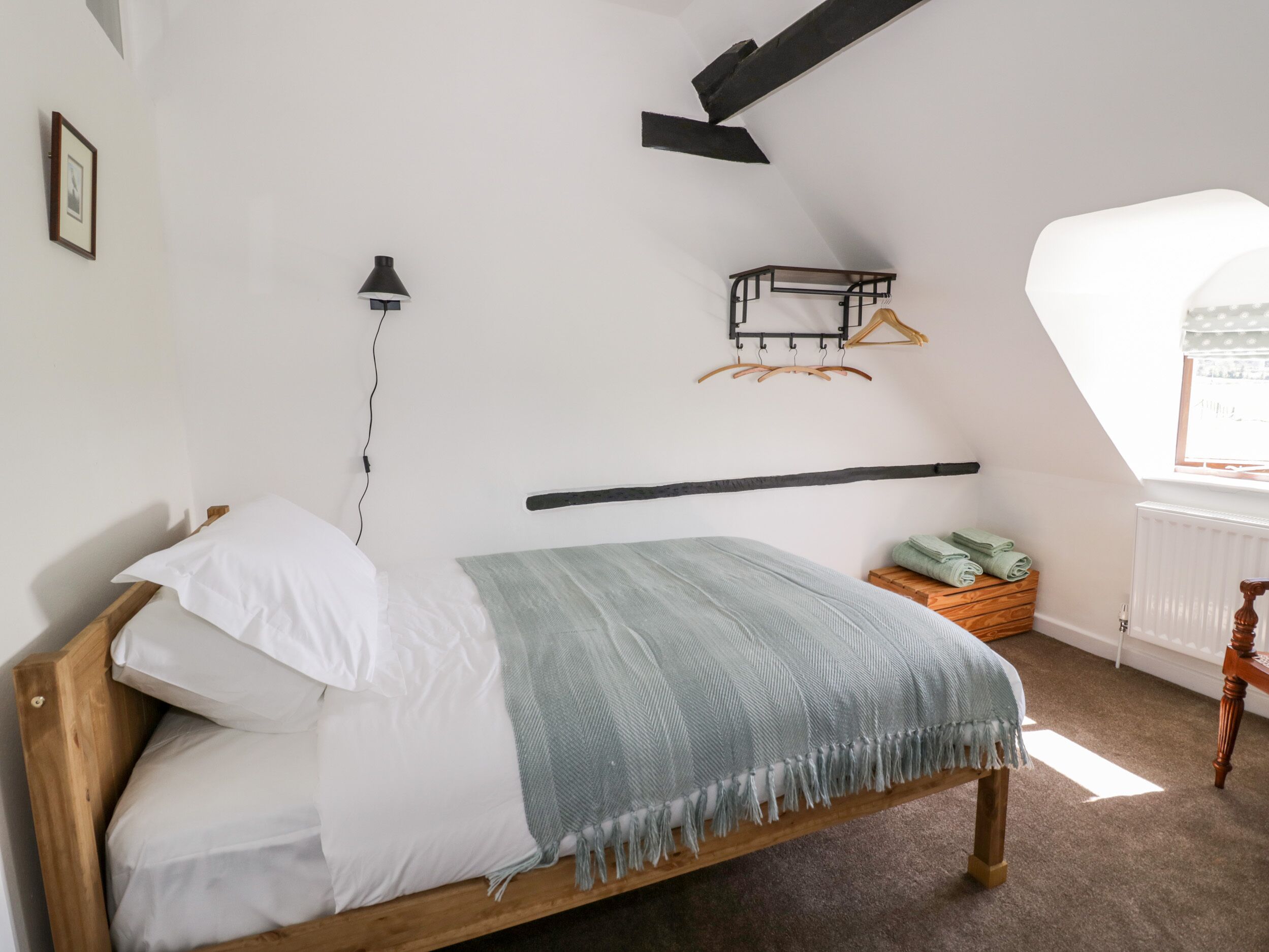 A bedroom with a wooden bed, a hanging light, a radiator, and a window with a view.