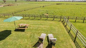 A grassy outdoor area with a wooden table and two lounge chairs, a green umbrella, and a wooden fence. - Manor Farm Cottage (Worcester)